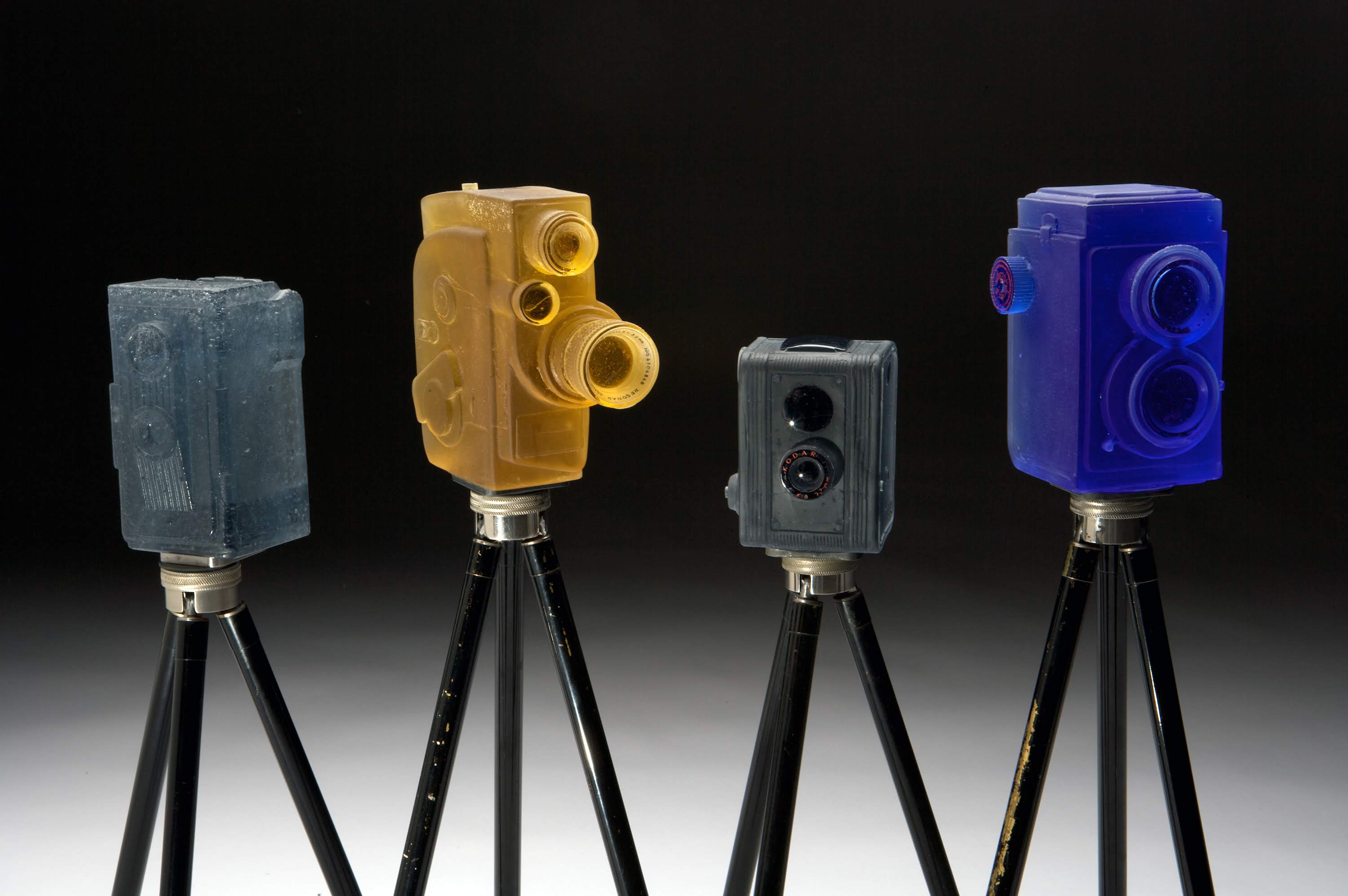 TITLE: Camera grouping “Imperial”, “Sekonic”, “Duaflex”, and “Reflex” DATE: 2012 SIZE: Size varies MEDIUM: Glass, antique Kodak tripod TECHNIQUE: Lost wax casting, painted, polished PHOTO: John Mueller
