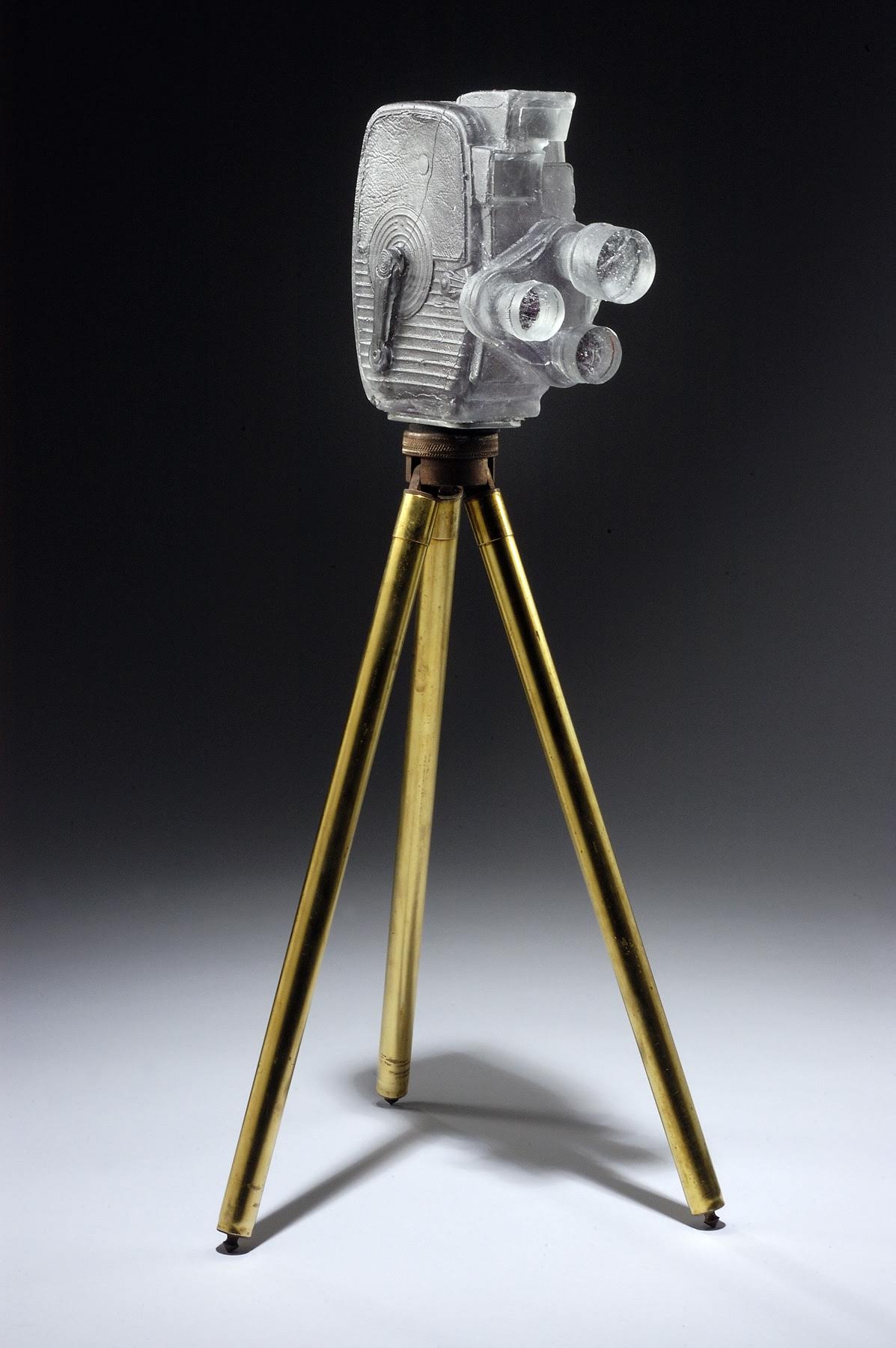 TITLE: “8mm” DATE: 2014 SIZE: 6"L x 5'W x 7"'H MEDIUM: Glass, antique tripod. TECHNIQUE: Lost wax casting, polished. PHOTO: Phocasso Photo